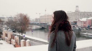 Arkadan Görünüm. Çekici genç esmer kız köprüde ayakta ve karla kaplı Kış town adlı görünüyor.