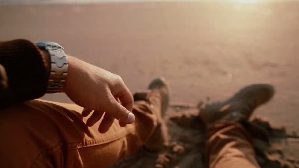 Une vidéo du premier point de vue d'un homme regardant un beau coucher de soleil en mer assis sur une plage de sable avec des bottes sur — Video