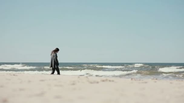 A young dark-haired pregnant woman is walking barefoot peacefully along the sea shore on a windy day. — Stock Video