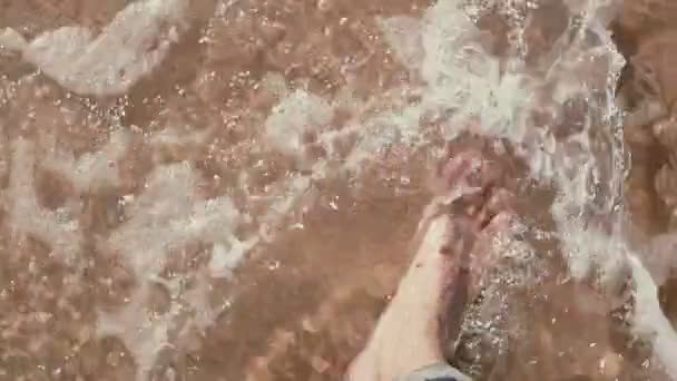 Een close-up van blote voeten van een man die is wandelen aan de kust met golven die naar zijn voeten. — Stockvideo
