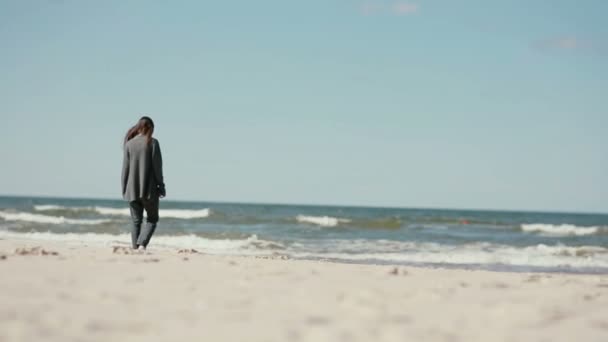 Een jonge dark-haired zwangere vrouw is blootsvoets lopen op een zandstrand op een koele dag. — Stockvideo