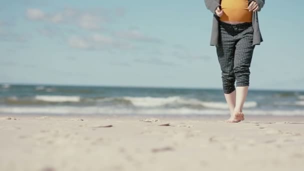 Hamile bir kadın çıplak ayakla yavaş yavaş kameraya yaklaşırken kumlu bir plaj üzerinde yürüyor. — Stok video