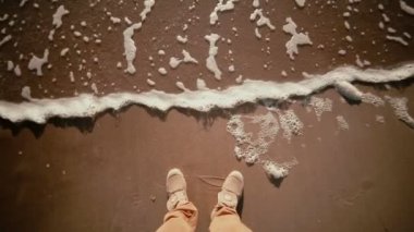 Yakın çekim onun ayaklarına gelen dalgalar ile kumlu bir kıyıda duran adam s çizme.