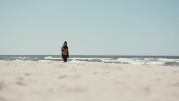 A young dark-haired pregnant woman is having a peaceful walk along the sea shore on a windy day. — Stock Video