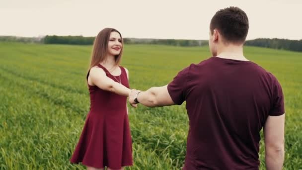 A man and a woman are joining hands, walking in a field, hugging and kissing. Slow mo, steadicam shot. — Stock Video