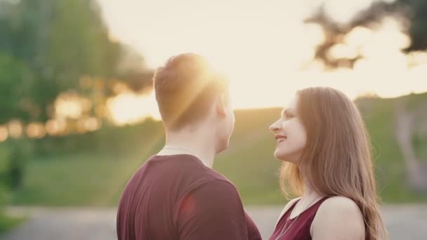 Jóvenes amantes se paran uno frente al otro al atardecer. Sonríen, el hombre toca suavemente su cabello, la mujer sacude el cabello. Lento mo — Vídeo de stock