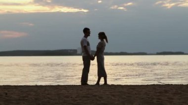 Gün batımında aşık genç bir çift silüeti. Kız durdu gezinemem ve yavaşça göl kıyısında adam öpücük