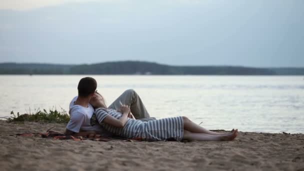 Young beautiful couple lying on the shore of the lake at sunset — Stock Video