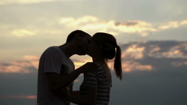 Силует молодої пари закоханої на заході сонця. Хлопчик цілує і обіймає свою дівчину на березі озера — стокове відео