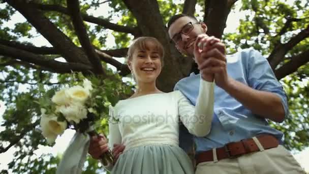 Vista de abajo. Joven hermosa recién casados besar contra un fondo de árbol verde en el parque — Vídeo de stock