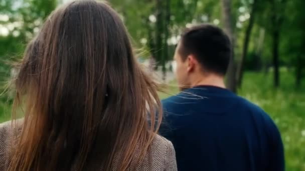 Back view of romantic young couple in love walking in park. Steadicam shot slow mo — Stock Video