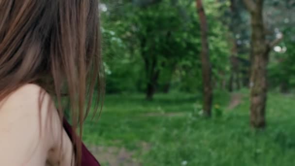 Rückansicht eines brünetten Mädchens mit langen Haaren, das im Garten oder Wald spazieren geht und Blätter von Bäumen berührt. slow mo, steadicam shot — Stockvideo
