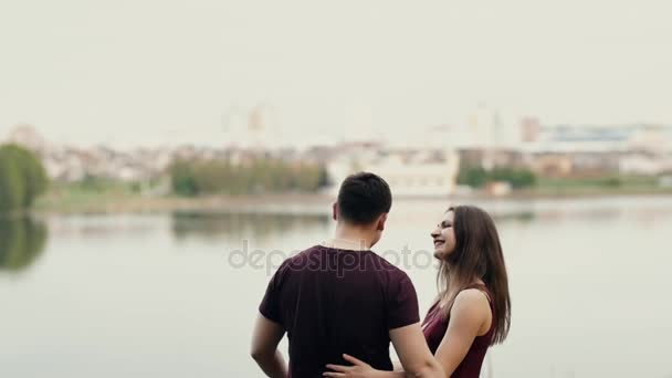 Backview of a happy couple enjoying view of city skyline, embracing each other. They hug, talk and smile. Slow mo — Stock Video
