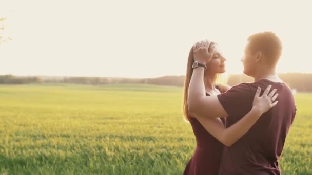 Happy man and woman in love stand in a field at sunset. They embrace and kiss, gently touch each other. Slow mo — Stock Video