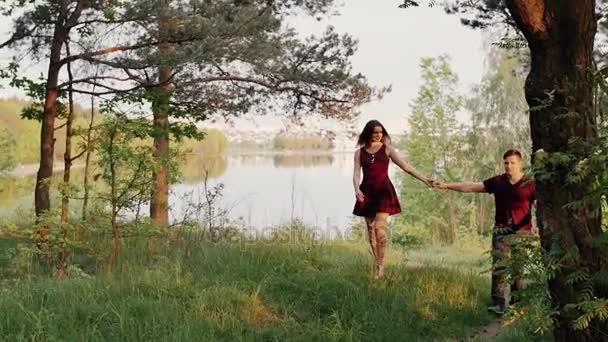 Happy couple walk on river bank, hold hands. Forest in summertime. Beautiful view of nature. Slow mo, steadicam shot — Stock Video