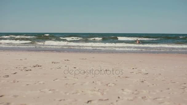 Uma vista distante de um homem pulando na água das ondas do mar em um dia ventoso . — Vídeo de Stock