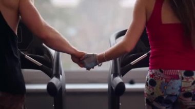 Arkadan Görünüm sportif bir çift el ele tutuşarak koşu bandı üzerinde çalışan. Eller close-up. Bir spor salonunda egzersiz.