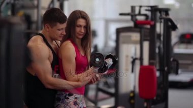 Sportif kadın spor kulübünde dışarı çalışırken halter kaldırıyor. Atletik adam ona doğru egzersiz yapmak için yardım.