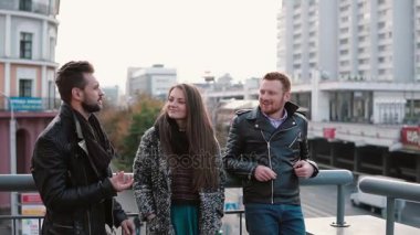Köprüde konuşmak iki yakışıklı delikanlı ve güzel bir kız. Arkadaş sohbet ve gülümseme, yolda araçların görünümü. Yavaş mo