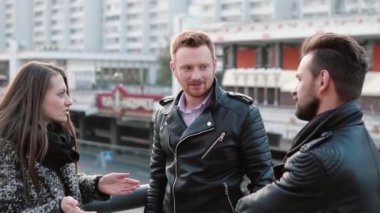 İki yakışıklı erkekler ve güzel bir kız ayakta bir köprü korkuluk yakınındaki konuş. Kız şaşırır, o zaman gülümsüyor. Yavaş mo
