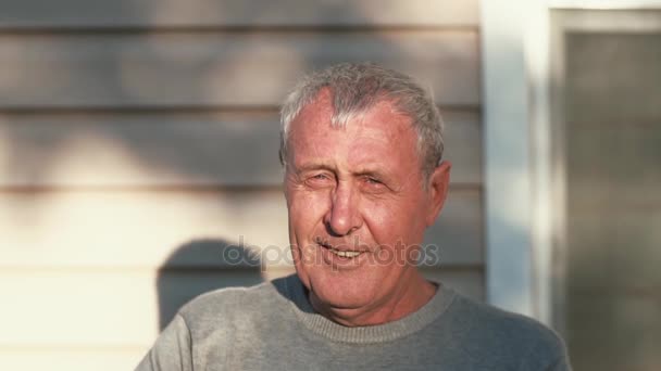 Egy idős férfi néz a kamerába, árnyalatok a szemét a nap, mosolyog. Lassú mo — Stock videók