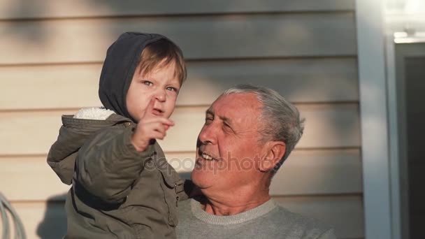 Старик держит маленького симпатичного мальчика на руках, смотрит на него. Мальчик указывает пальцем на что-то. Медленно — стоковое видео
