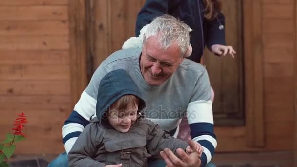 Стареющий мужчина прекрасно проводит время со своими внуками. Он обнимает их, они счастливо бегают вокруг. Медленно — стоковое видео