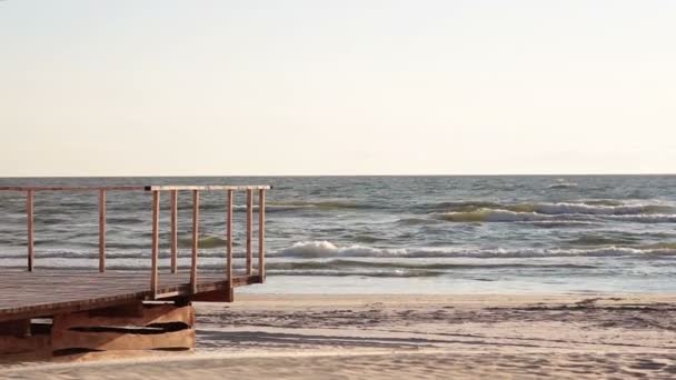 Widok z brzegu morza w wietrzny dzień, kiedy fale przyjść na pokład drewniany wybudowany na plaży. — Wideo stockowe