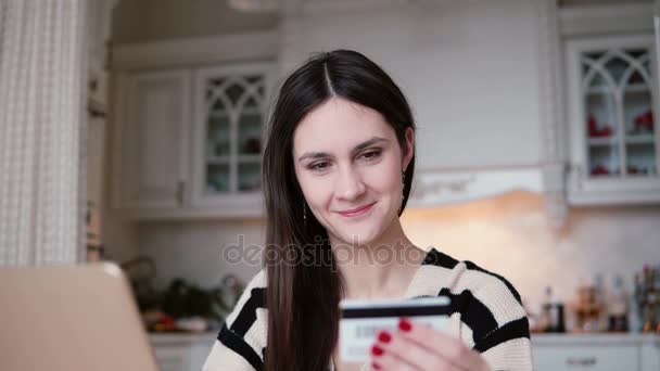 Attraente giovane oman sorridente utilizza la carta di credito di plastica shopping online con il computer portatile. Macchina fotografica lento si muove per ragazza — Video Stock