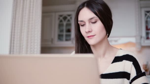 Porträt einer schönen jungen brünetten Frau mit Laptop in einem hellen Esszimmer. — Stockvideo