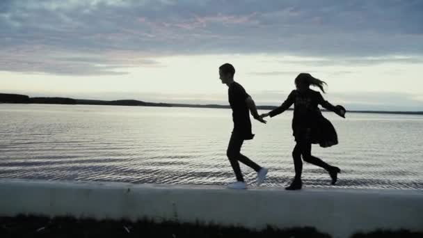 Joven hombre y chica corriendo a lo largo del terraplén al atardecer, cámara lenta — Vídeos de Stock