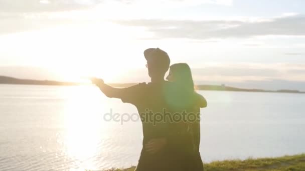 Pasangan muda dan gadis jatuh cinta berjalan di sepanjang tepi pantai saat matahari terbenam — Stok Video