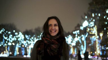 parlak ışıklar, kamera önünde park ağaçlar bakarak karlı Noel gecesi smiles çekici kadın dekore