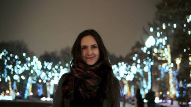 parlak ışıklar, kamera önünde park ağaçlar bakarak karlı Noel gecesi smiles çekici kadın dekore