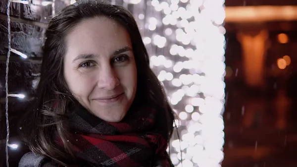 若い魅力的な女性ライト壁際カメラ立って見てクリスマスの夜に雪が降る, — ストック写真