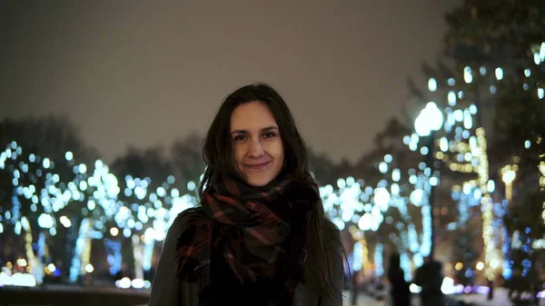 公園の木の前でカメラを見て雪のクリスマス夜笑顔で魅力的な女性装飾輝くライト — ストック写真