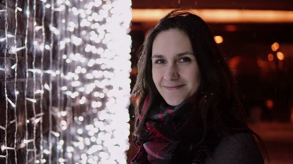 背景にカメラのライトを見てクリスマスの夜に雪が降るの若い魅力的な女性 — ストック写真