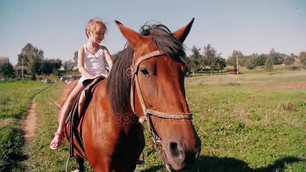 Una niña feliz montando un caballo en un camino rural en un día soleado. Ella sonríe, se divierte. Lento mo , — Vídeos de Stock