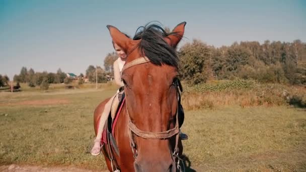 Una bambina sorridente che cavalca un cavallo in campagna in una giornata estiva soleggiata. Lento mo — Video Stock