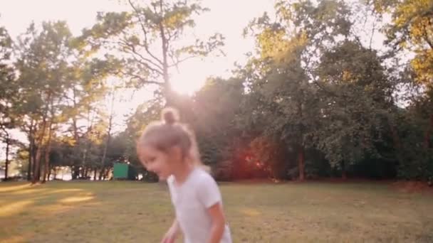 Gelukkig klein meisje blaast kussen voor camera in de natuur. Zonsondergang, lichtstralen van de zon schijnen door bomen. Slow mo — Stockvideo