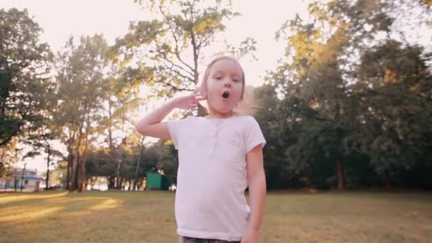 Happy little girl cheerfully jumps, blows kisses in front of camera in the nature. Beautiful sunset light. Slow mo — Stock Video