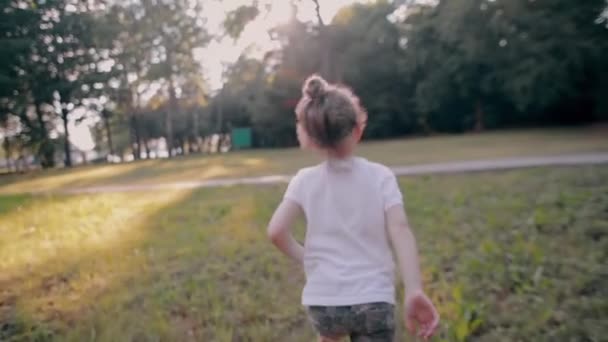 Веселая маленькая девочка убегает от камеры на природе в солнечный летний день. Вид сзади, медленное движение — стоковое видео