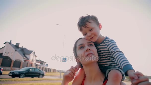 A mãe e o filho são felizes juntos num dia ensolarado. O menino bonito senta-se nos ombros das mães. Devagar. — Vídeo de Stock