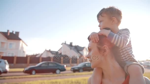 Vista lateral da família passar o tempo juntos em um dia ensolarado de verão. O menino bonito senta-se nos ombros das mães. Devagar. — Vídeo de Stock