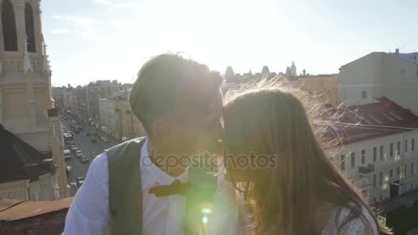 Felice giovane bella coppia elegante sposa e sposo bacio delicatamente sul tetto al tramonto strada della città sullo sfondo — Video Stock