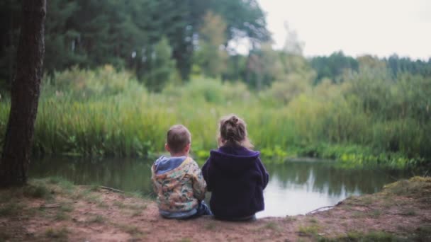 2 つの小さな子供、女の子と川の土手に座っている男の子。女の子がスイカを食べて、彼らは振り返る。Backview — ストック動画