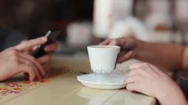 Genç kadın kahve içme yan görünüm. Kadının bir fincan kahve var. Onun akıllı telefon kullanan bir adam elinde.