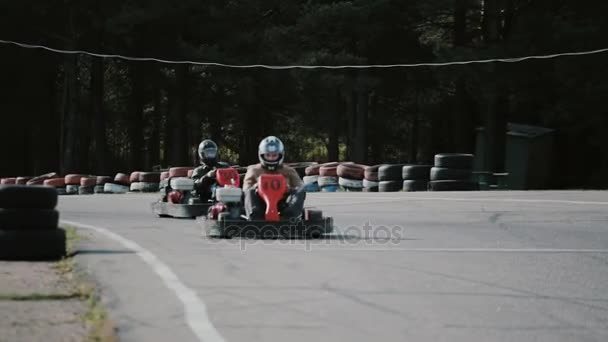 Conductores de karts moviéndose en una pista de karts pasando por la cámara . — Vídeo de stock