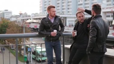 Üç genç yakışıklı adam sakallı bir köprü korkuluk görüşme. Yakışıklı çocuklar konuş, kahve iç. Yavaş mo