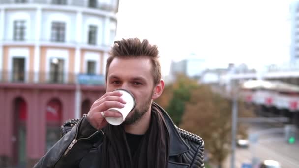 Een stijlvolle knappe man met een baard drinken afhaalmaaltijden koffie of thee op zoek naar de kant. — Stockvideo